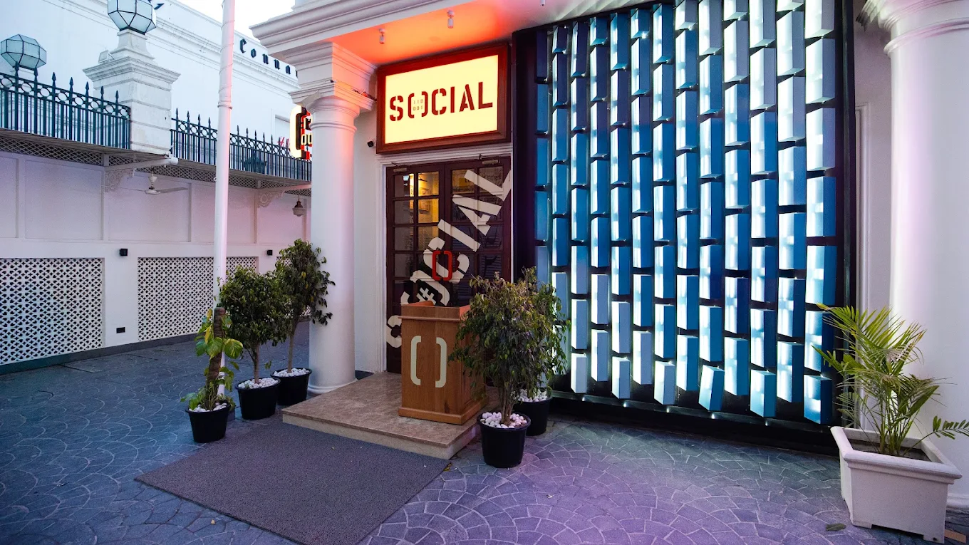 Entrance of SOCIAL, one of the romantic restaurants in Delhi, with a glowing signboard, white colonnade and a blue illuminated façade