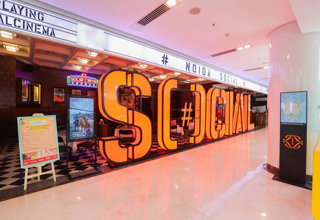 Large glowing orange SOCIAL letters at the Noida SOCIAL entrance, with a cinema-style marquee and checkered floor
