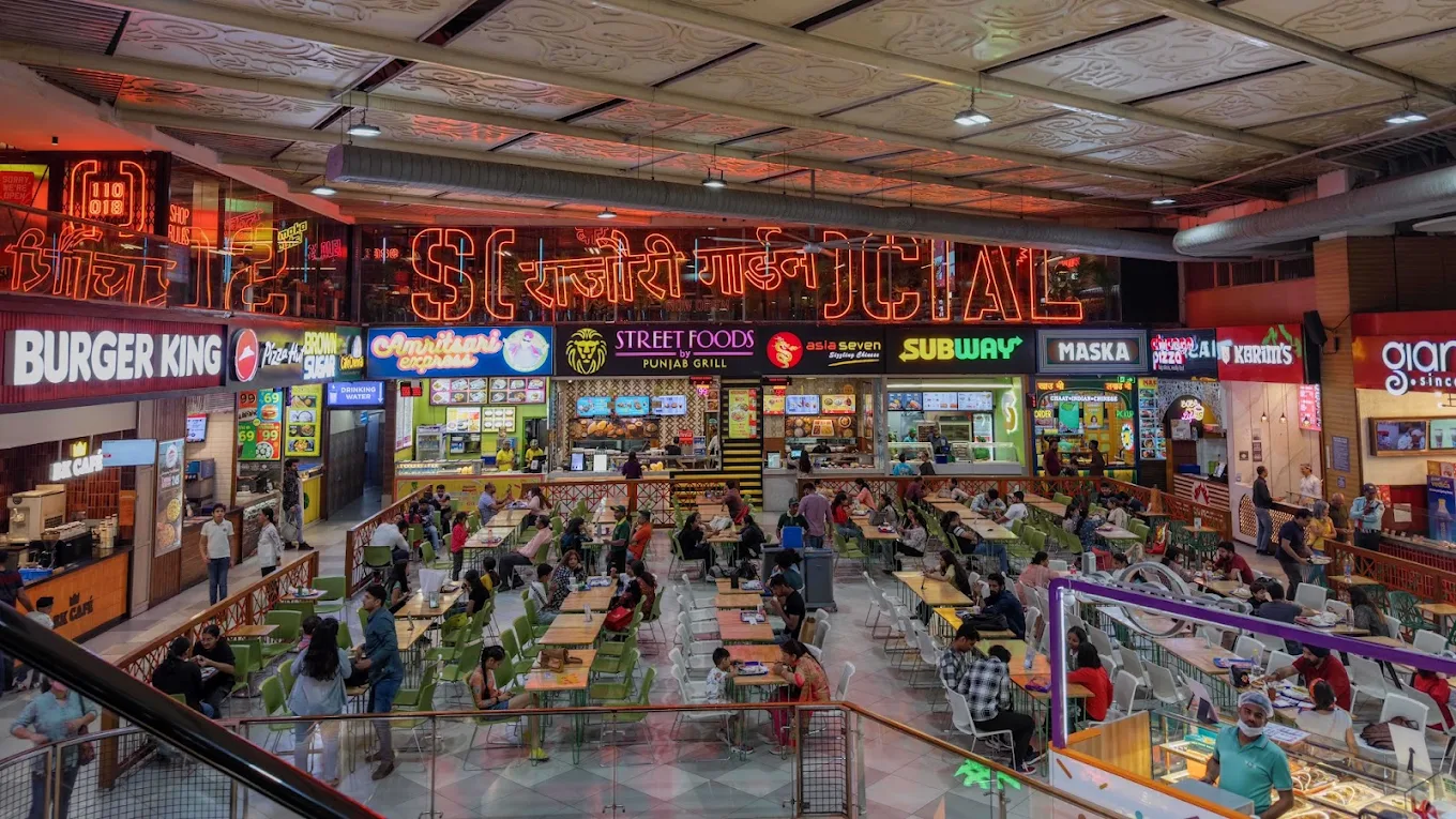 Crowded food court with neon signage and fast-food outlets, an affordable cafe in Rajouri Garden